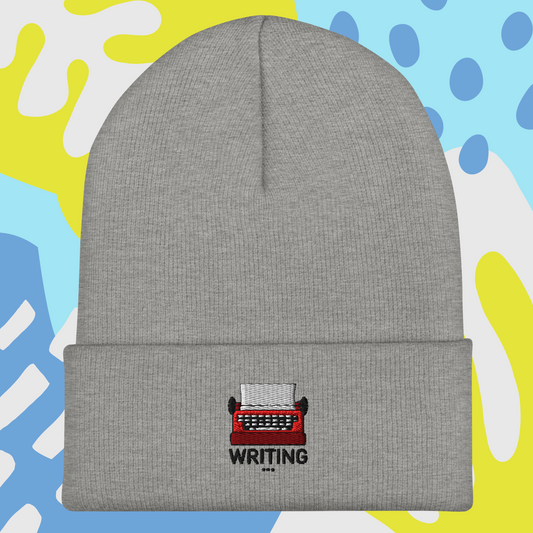 Gray beanie with a red typewriter and 'WRITING' text embroidery on a colorful abstract background